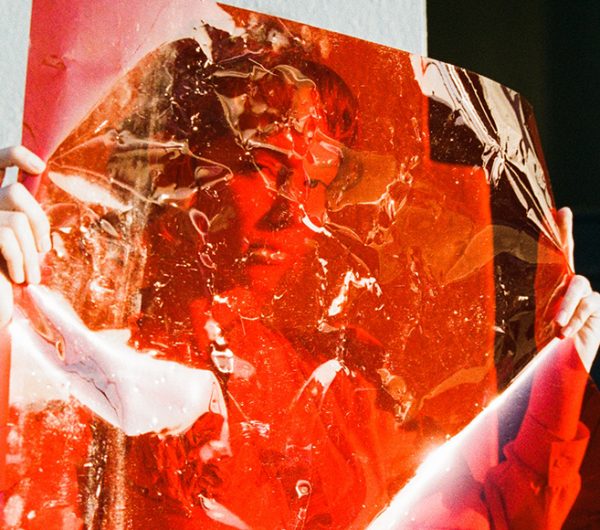 A woman is shown hiding behind a transparent red foil or film