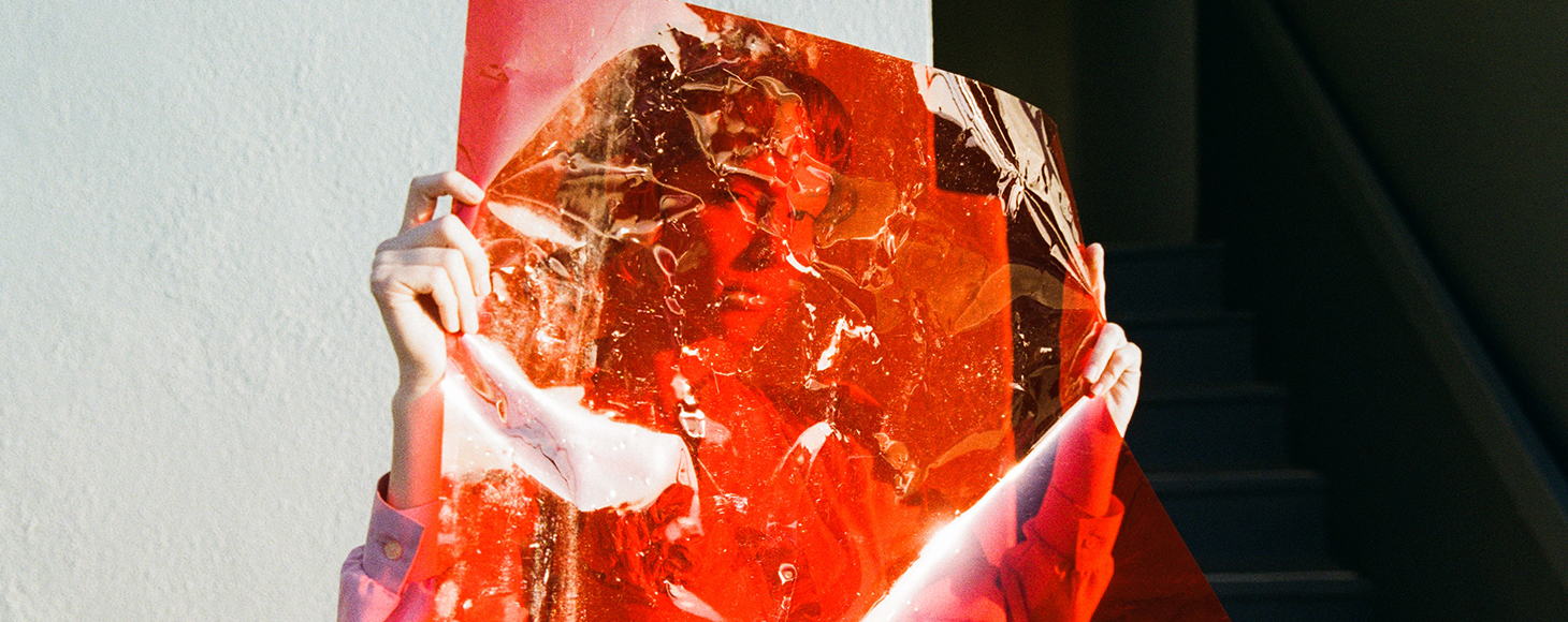 A woman is shown hiding behind a transparent red foil or film